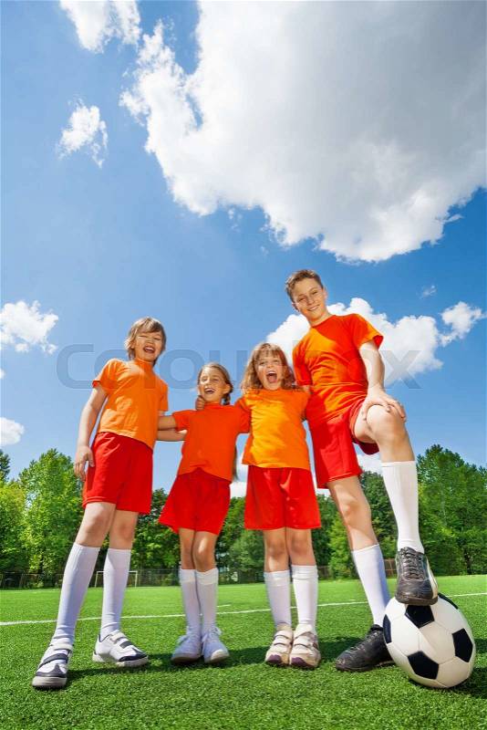 Laughing children of different height with football standing in a row on football field, stock photo