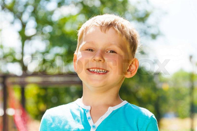 Close portrait of the little Caucasian happy boy in blue outside in the park with big toothy smile, stock photo