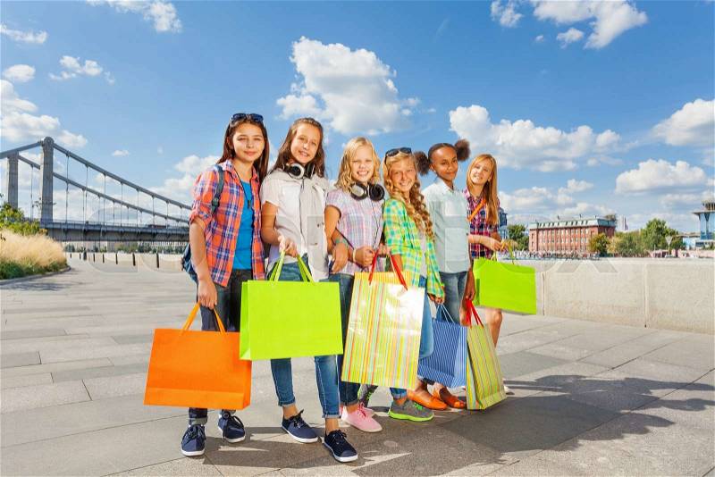 Friends with shopping bags walk together arm-in-arm in the city and smile happily in summer during daytime, stock photo