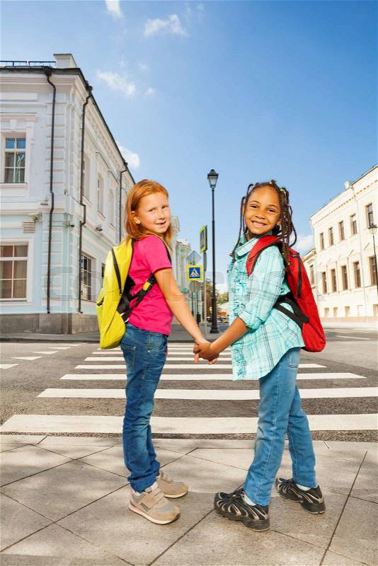 Two girls holding hands and standing near crossroad and smile in city during summer, stock photo