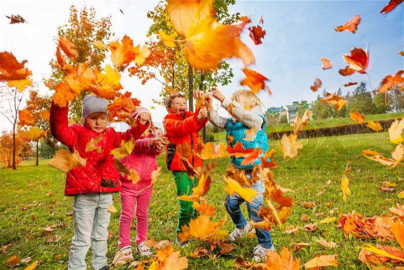 Active group of children playing with flying maple leaves and enjoying wonderful autumn day, stock photo