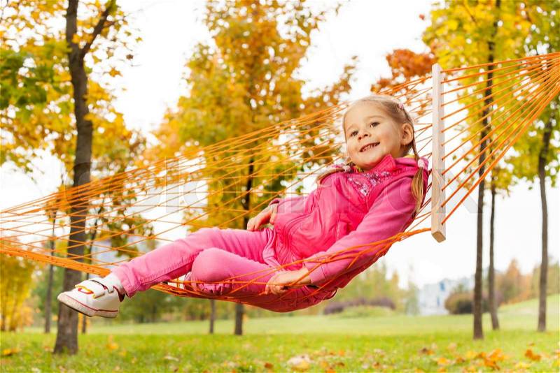 Blond girl laying on net of hammock in the park during beautiful autumn day, stock photo