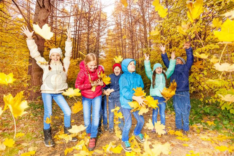 Happy excited kids playing together with flying yellow leaves in forest during autumn daytime, stock photo