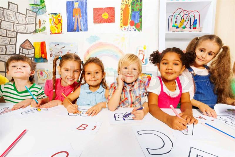 Group of diverse looking boys and girls in kindergarten class drawing letters in early reading class, stock photo