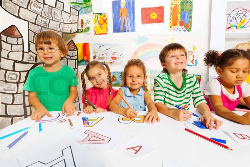 Happy group of kids drawing and filling letters on the paper in the early reading class, stock photo