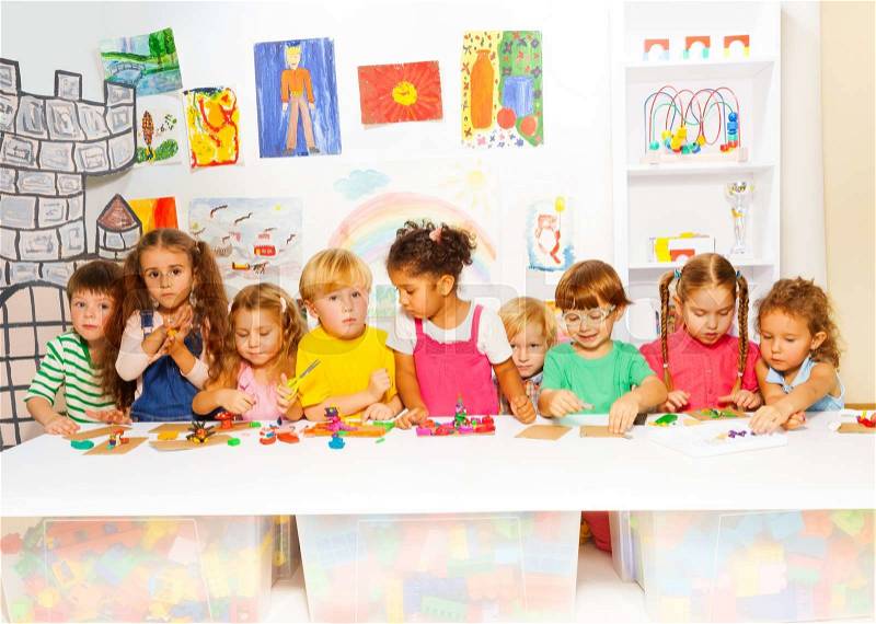Large group of diverse looking kids, boys and girls in the kindergarten class play with modeling clay, stock photo