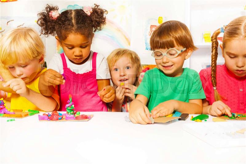 Group of kids in the kindergarten play with modeling clay in the class, stock photo