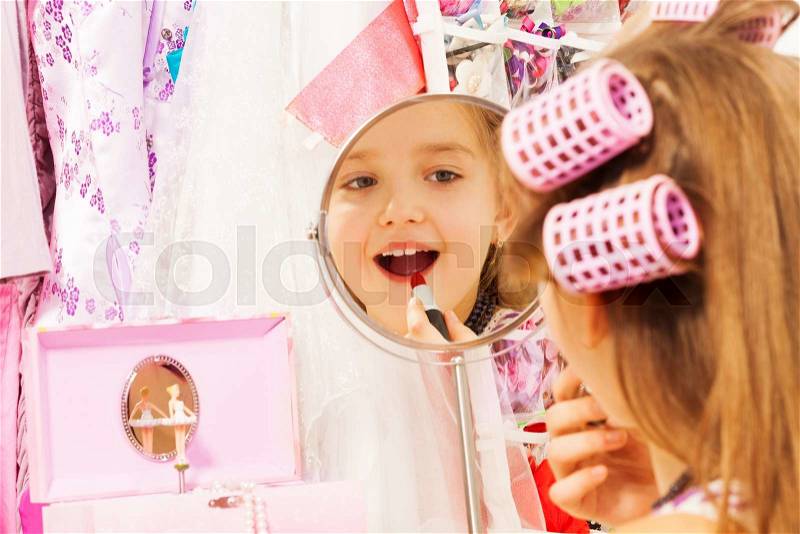 Beautiful girl making up her face and reflecting in round mirror while sitting turned back with accessories on background, stock photo
