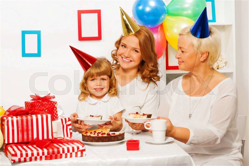 Happy smiling family by the table on children girls birthday eating birthday cake with many present near, stock photo