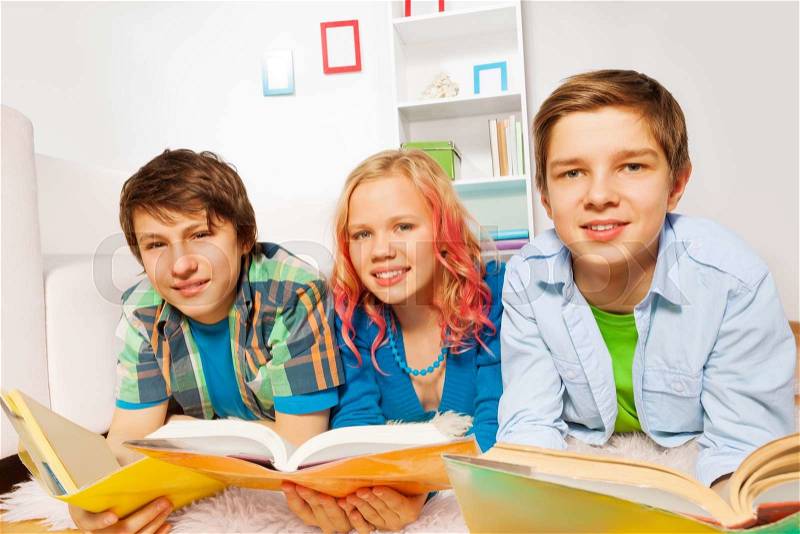 Two boys and beautiful young teen girl laying on the floor studying with books happy and smiling , stock photo