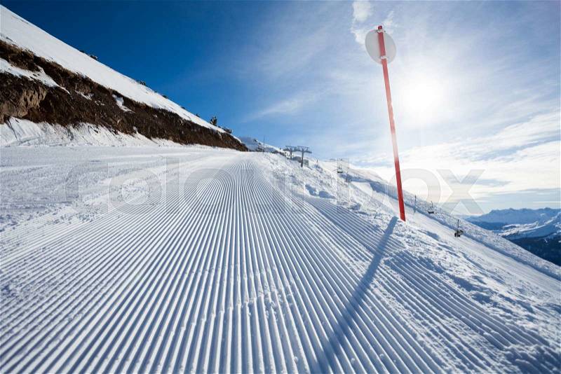 Winter landscape of long ski-track with sign and fragment of Caucasus mountains during sunny day in Sochi ski resort Krasnaya polyana, Russia, stock photo