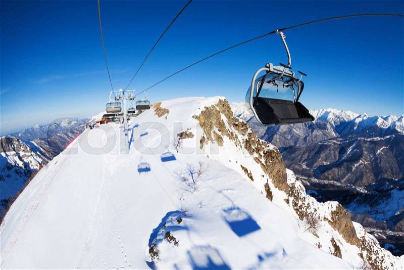 Ski lift chairs over the mountain peak with piste bellow on sunny winter day, stock photo