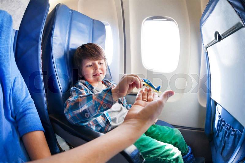 Little boy takes little plane from moms hand sitting by the window in jet airplane , stock photo