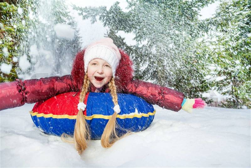 Excited girl on snow tube in winter during day in the fir tree forest, stock photo