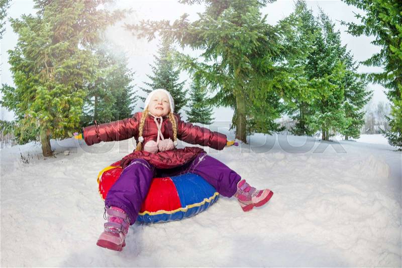 Girl sitting on snow tube relaxed in winter during day in the fir tree forest, stock photo