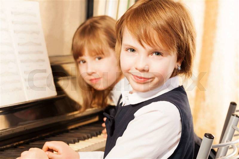 Close-up view of two cheerful beautiful small girls playing piano together with notes during lesson, stock photo