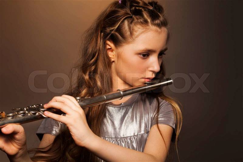 Close-up view of girl with long hair holding and playing on silver flute over gel colored dark background, stock photo