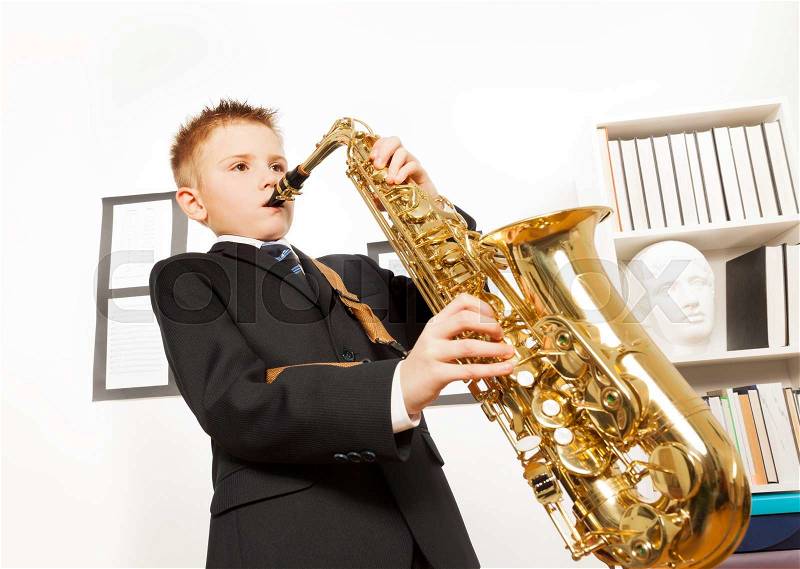 Boy in school uniform playing on alto saxophone close-up view in musical school, stock photo