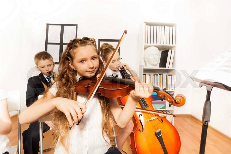 Performance of cheerful children playing musical instruments together in musical school, stock photo