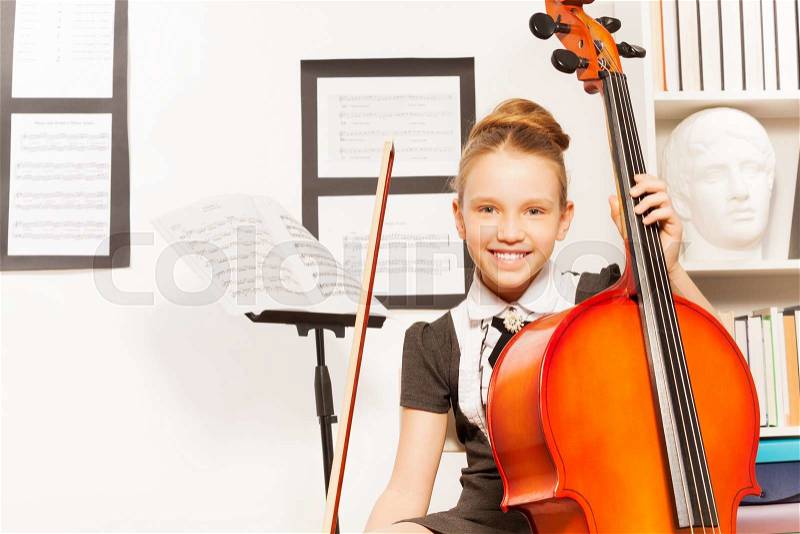 Smiling girl holding the string to play violoncello indoors, stock photo