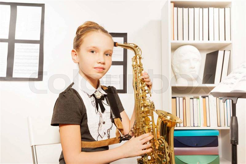 Portrait of girl in school uniform dress with alto saxophone to play in musical school, stock photo