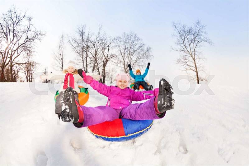 Girl with legs up and her friends sliding down the hill on the tubes with arms up during beautiful winter day , stock photo