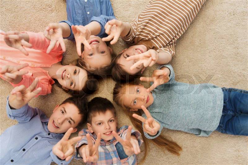 Childhood, fashion, friendship and people concept - happy smiling children showing peace hand sign and lying on floorin circle, stock photo