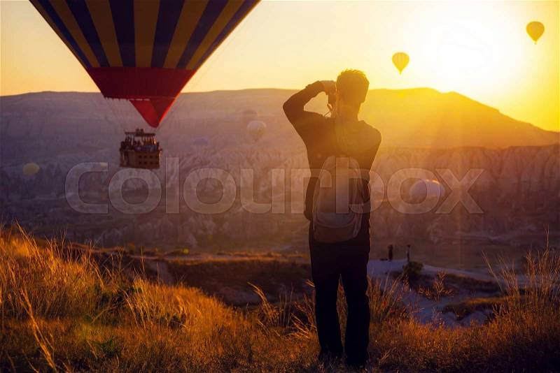 Man taking picture of Hot air balloons flying over spectacular Cappadocia, stock photo