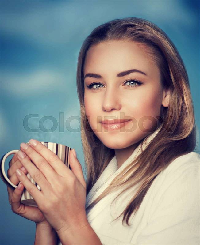 Portrait of beautiful blond woman with coffee cup in hands over blur blue sky background, enjoying morning energetic drink, stock photo