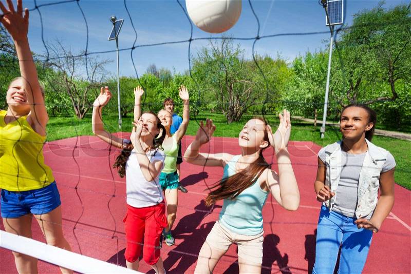 Teenagers in team play volleyball on the court during sunny summer day outside, stock photo