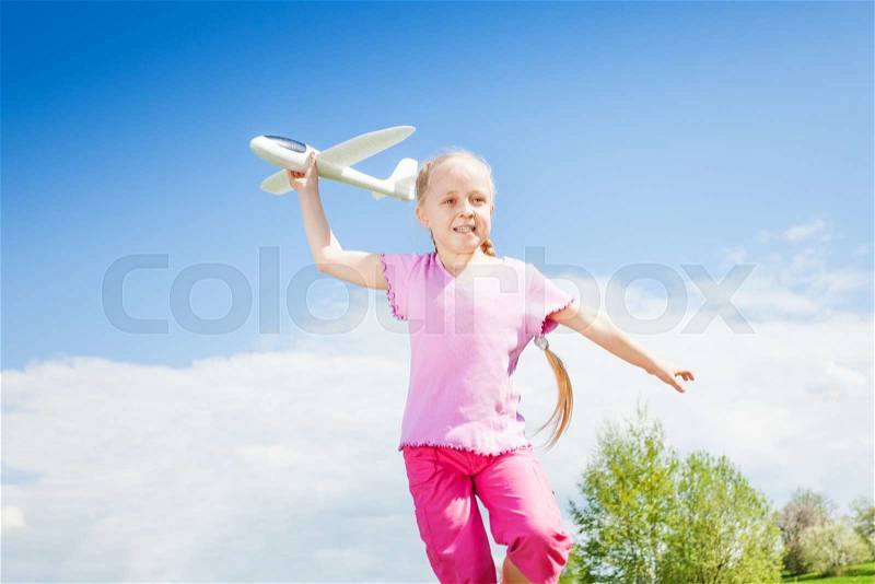 Happy smiling girl holding airplane toy during running in the green filed in summer time, stock photo