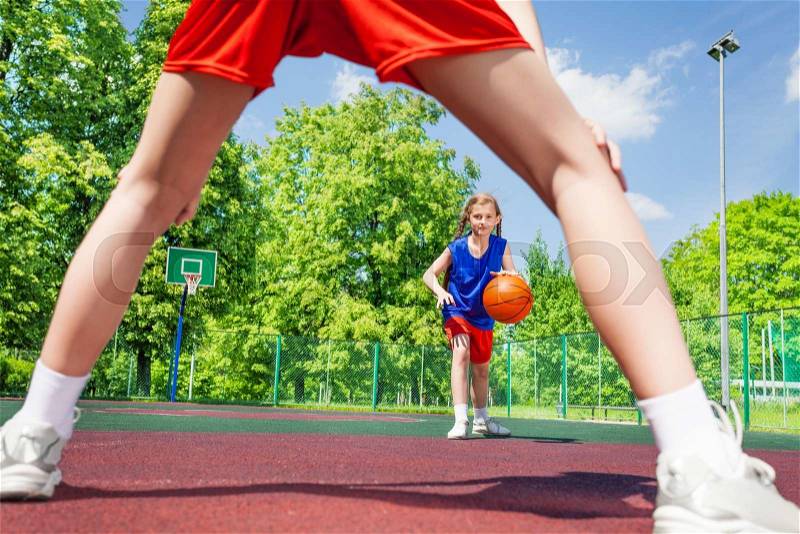 Girl with ball view between two legs of opposite player during basketball game on the playground outside, stock photo