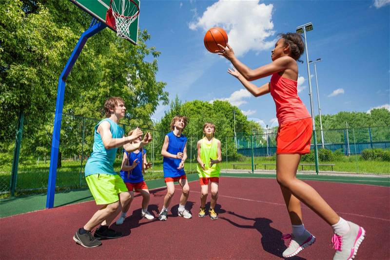 Teenagers are playing basketball game on the ground during sunny summer day together, stock photo