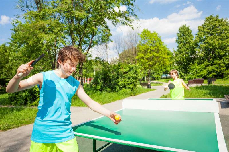 Boy with racket ready to play in table tennis game outside during summer sunny day, stock photo