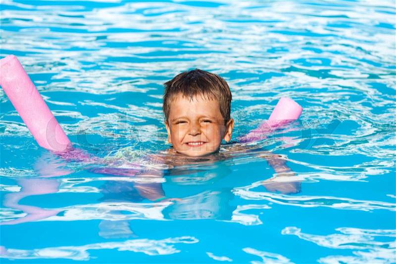 Happy small boy learns how to swim with pool noodle in swimming pool during summer, stock photo