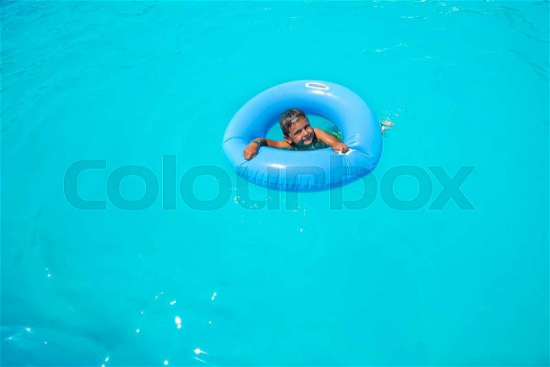 Happy small boy in inflatable ring swimming in pool outside during summer sunny day, stock photo