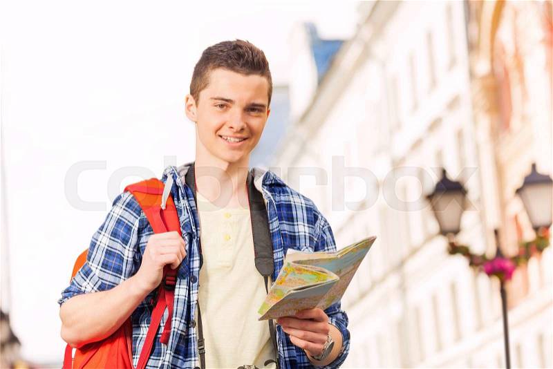 Boy with rucksack and city map on the street during summer vacation time in Europe, stock photo