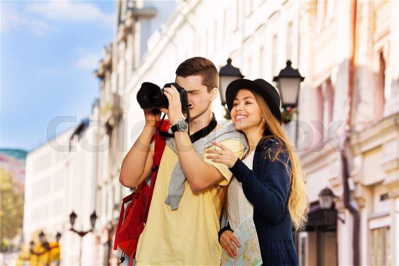 Young man shooting with camera and girl both as tourists sightseeing on the European street during summer day time, stock photo
