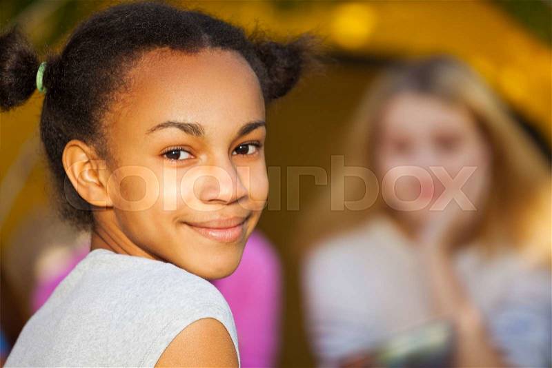 Happy African beautiful girl portrait sitting near yellow tent with her friends during sunny autumn day at campsite, stock photo