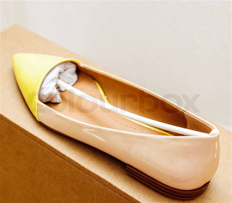 Yellow leather woman shoe placed on cardboard box in luxury retail shopping center with wooden parquet floor, stock photo