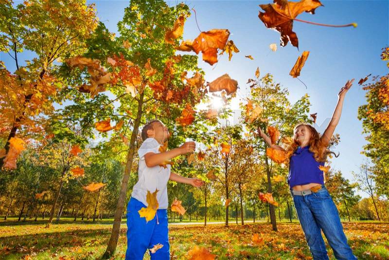 Two friends playing with thrown leaves in the forest together during beautiful autumn sunny day, stock photo