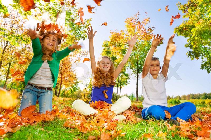 Children throw and play with leaves in the forest together during beautiful autumn sunny day, stock photo