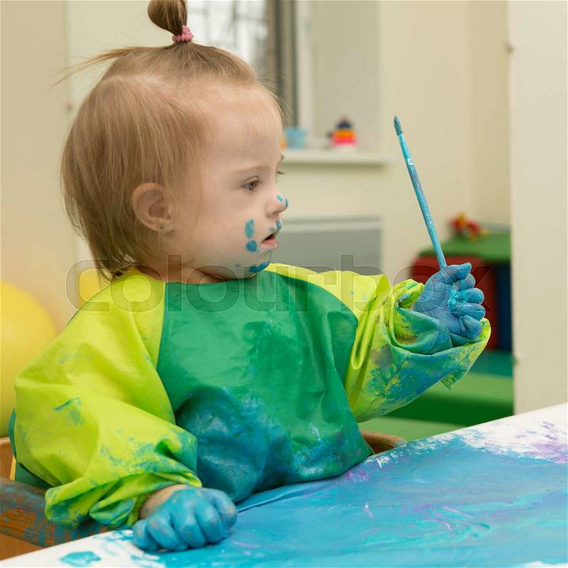 Girl with Down syndrome covered in paint when drawing, stock photo