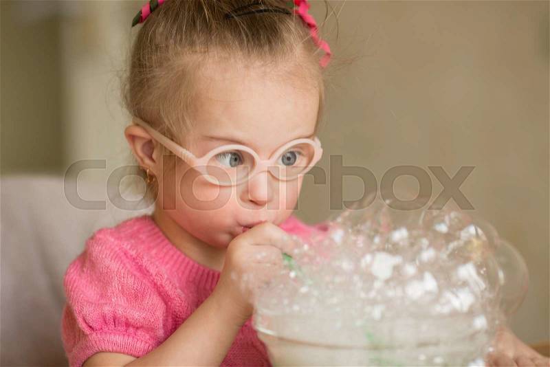Girl with Down syndrome makes breathing speech therapy exercise, stock photo