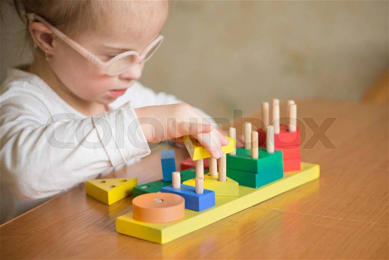 Beautiful girl with Down syndrome sorts geometric shapes, stock photo