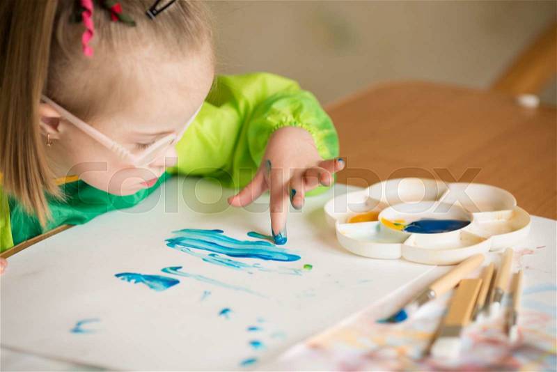 Girl with Down syndrome covered in paint when drawing, stock photo