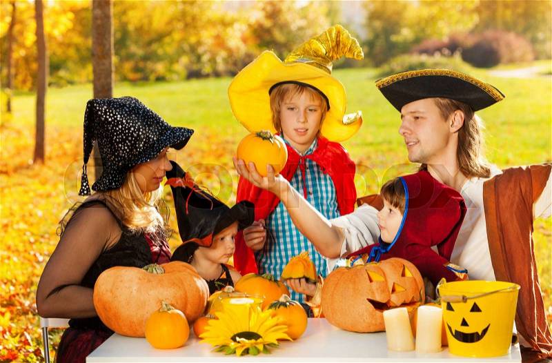 Family in Halloween costumes with Jack-O\'-Lantern pumpkin sitting at the table outside during beautiful sunny autumn day, stock photo