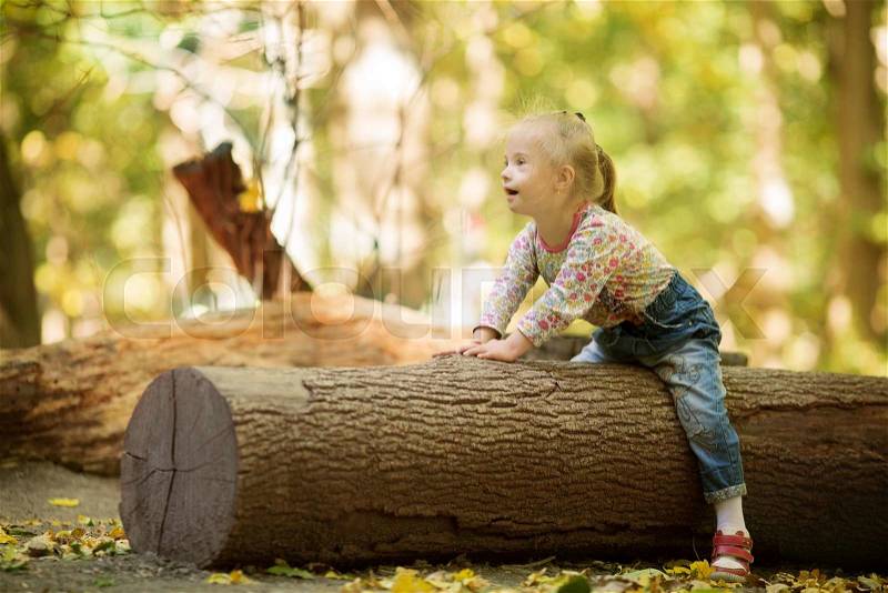 Funny little girl with Down syndrome sitting on a large log, stock photo