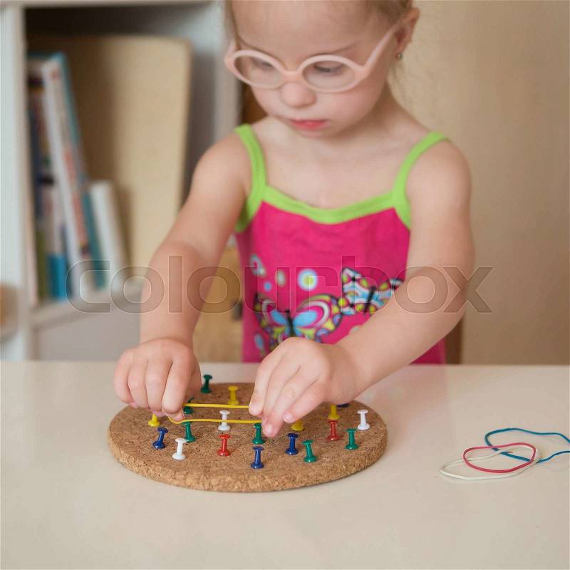 Girl with Down syndrome develops fine motor skills of hands, stock photo
