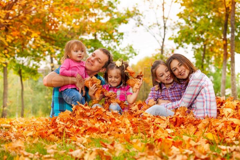 Happy family play with little daughters in the pile of autumn maple orange leaves in the park, stock photo